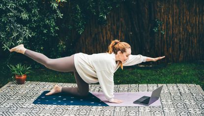 Woman doing Reformer Pilates at home on yoga mat in garden