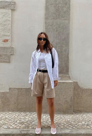 a photo of a woman's spring vacation outfit with a button-down shirt over a white tank styled with shorts and mesh flats