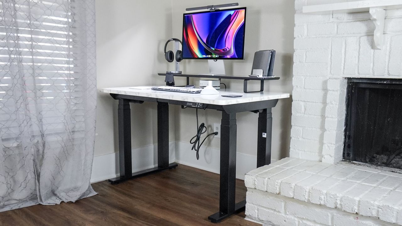 The FlexiSpot E7 Plus standing desk set up in a corner next to a fire place