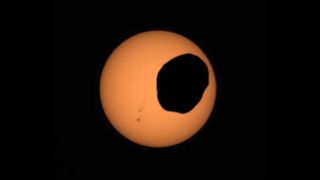 The silhouette of a rocky, lopsided moon passes in front of the sun