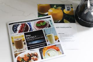 Ninja Detect Duo Power Blender Pro's easy recipes booklet and edge of smoothie attachment on a white marble counter with light gray veins