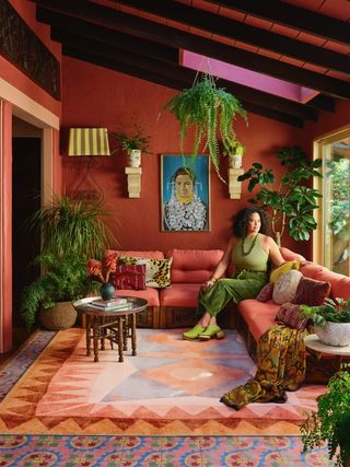 justina blakeney sitting in a colorful room with her rug collection, a red wall, timber ceiling