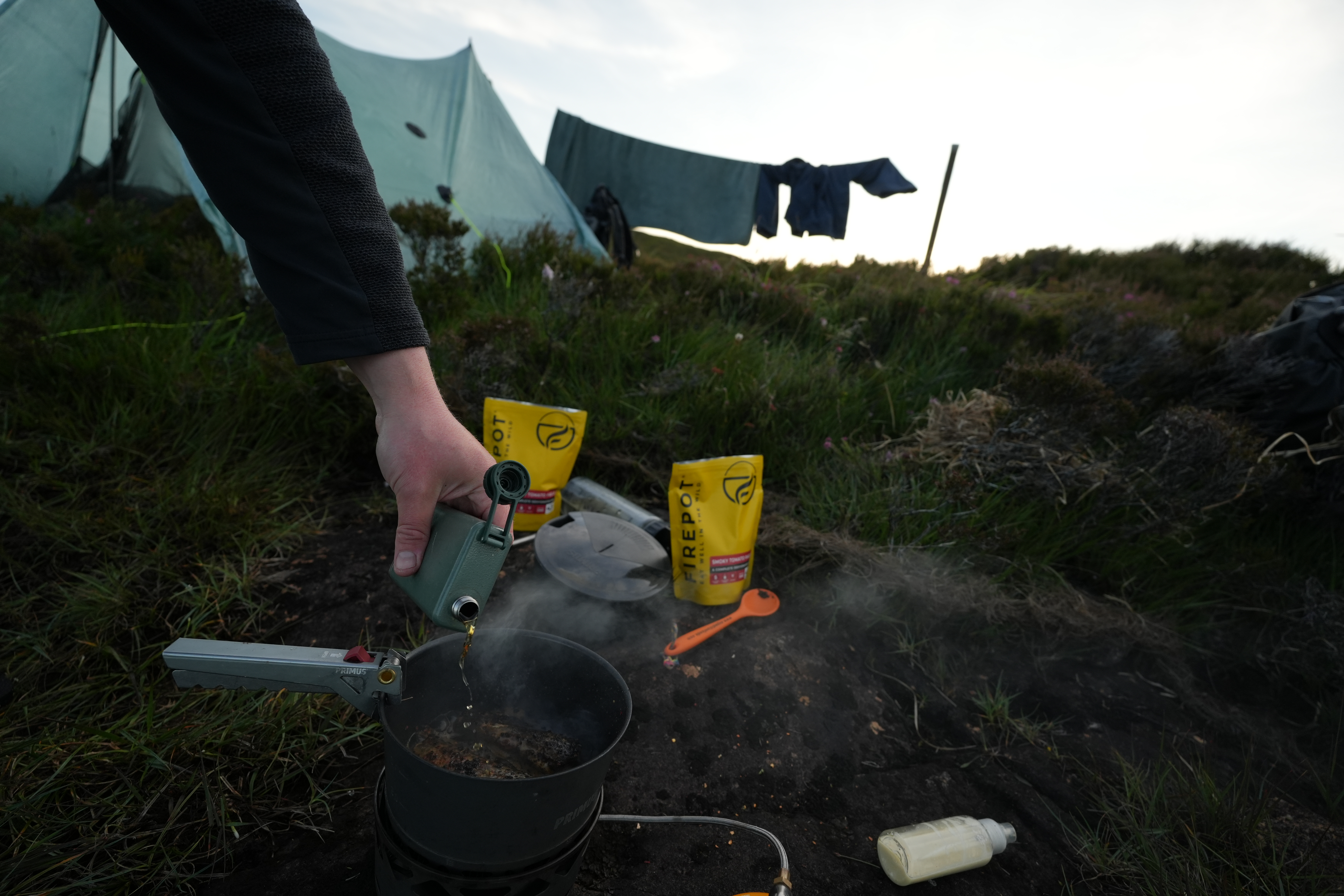 Whisky being poured into a pan of fish on an outdoor stove
