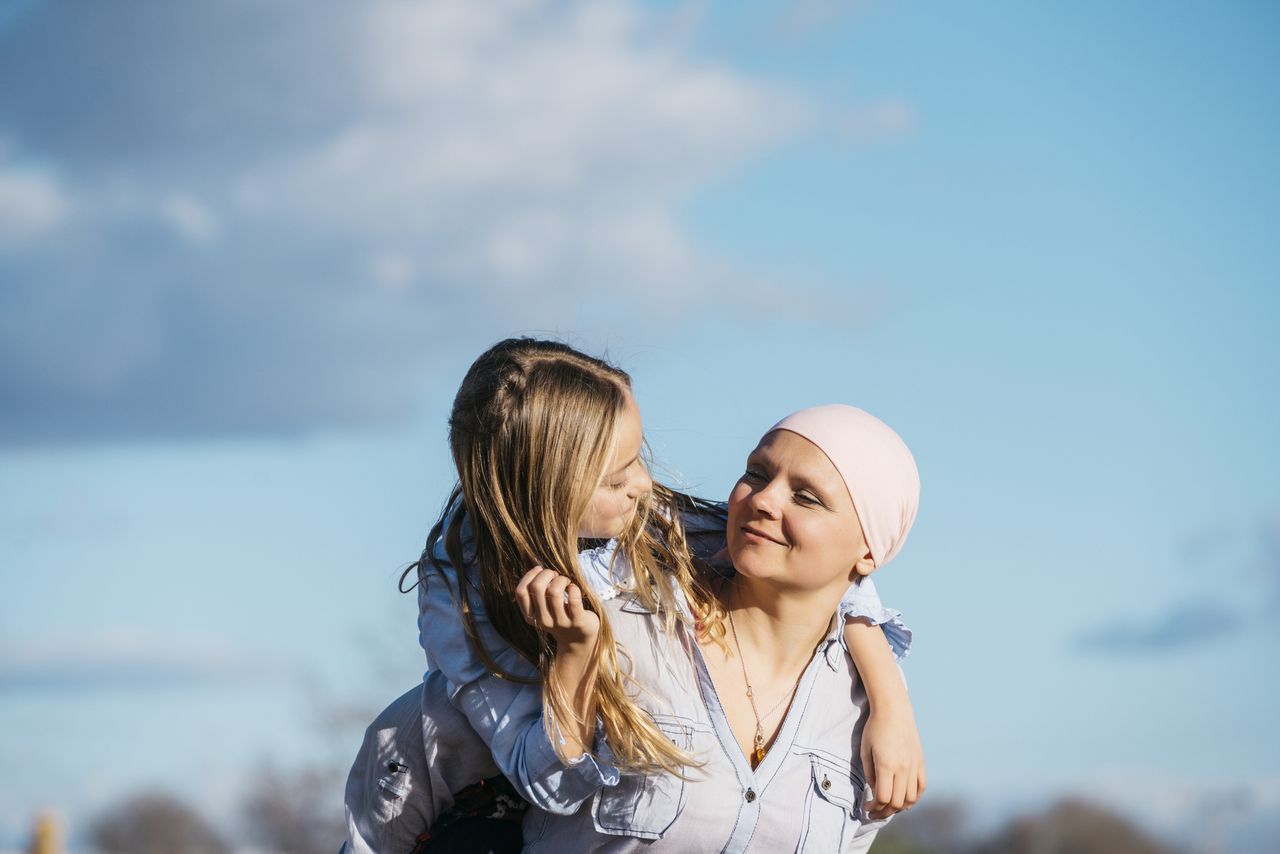 Cancer care: A woman with cancer is next to her daughter. A girl is hugging a woman happy