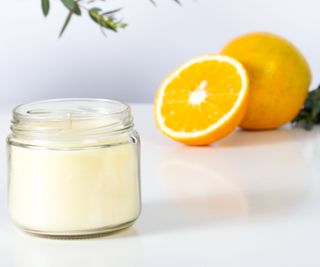 A white candle in a jar beside a sliced orange
