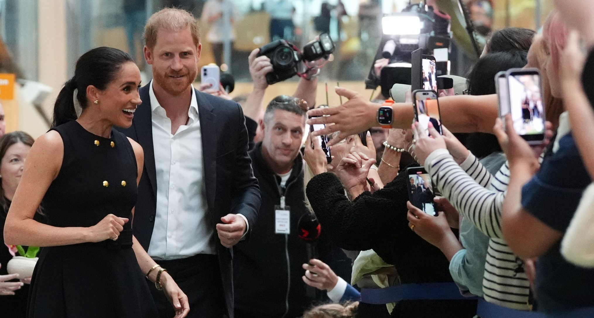 Meghan Markle and Prince Harry greeting a crowd of people taking their photos 