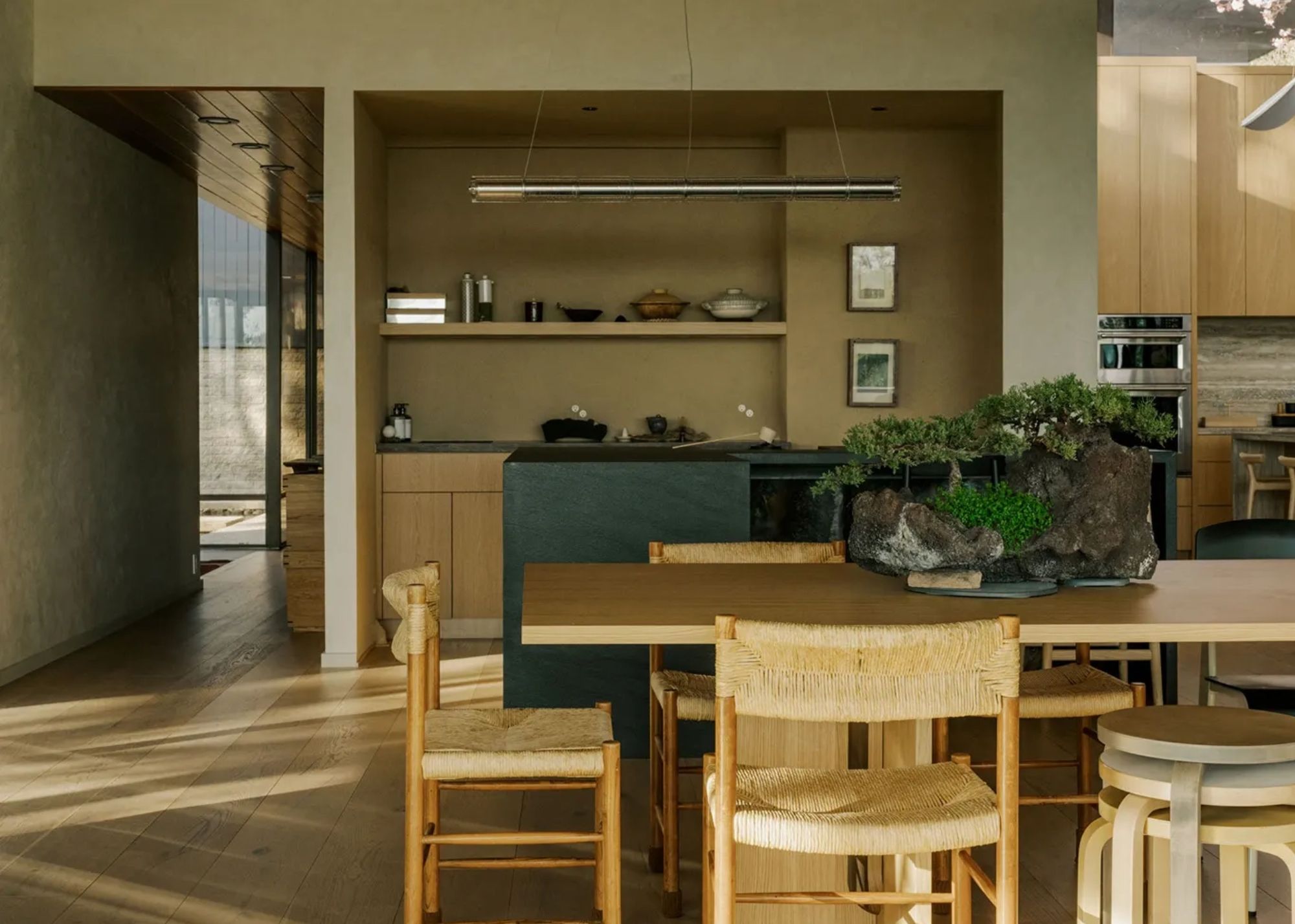 An open concept kitchen and dining room with minimalist design and a living centrepiece and dappled light