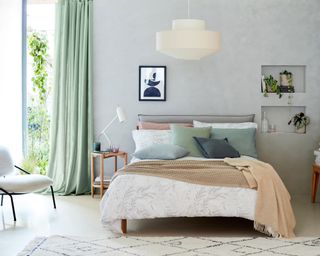 A bedroom with light grey chalk paint wall decor, mint green curtain decor, a bed with white botanical duvet, and two recess shelves