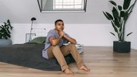 A man sits on a mattress on the floor before he falls asleep 