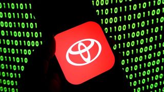 A silhouette holds a phone with the Toyota logo on it, with green binary code in the background