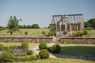 oak frame greenhouse with brick retaining wall and landscaped garden