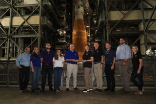 Cliff Lanham, fifth from the left, ground operations manager with NASA's Exploration Ground Systems (EGS), hands off the baton to Charlie Blackwell-Thompson, Artemis I launch director, on Aug. 15, 2022. Also pictured are members of Kennedy's EGS and Artemis launch teams.