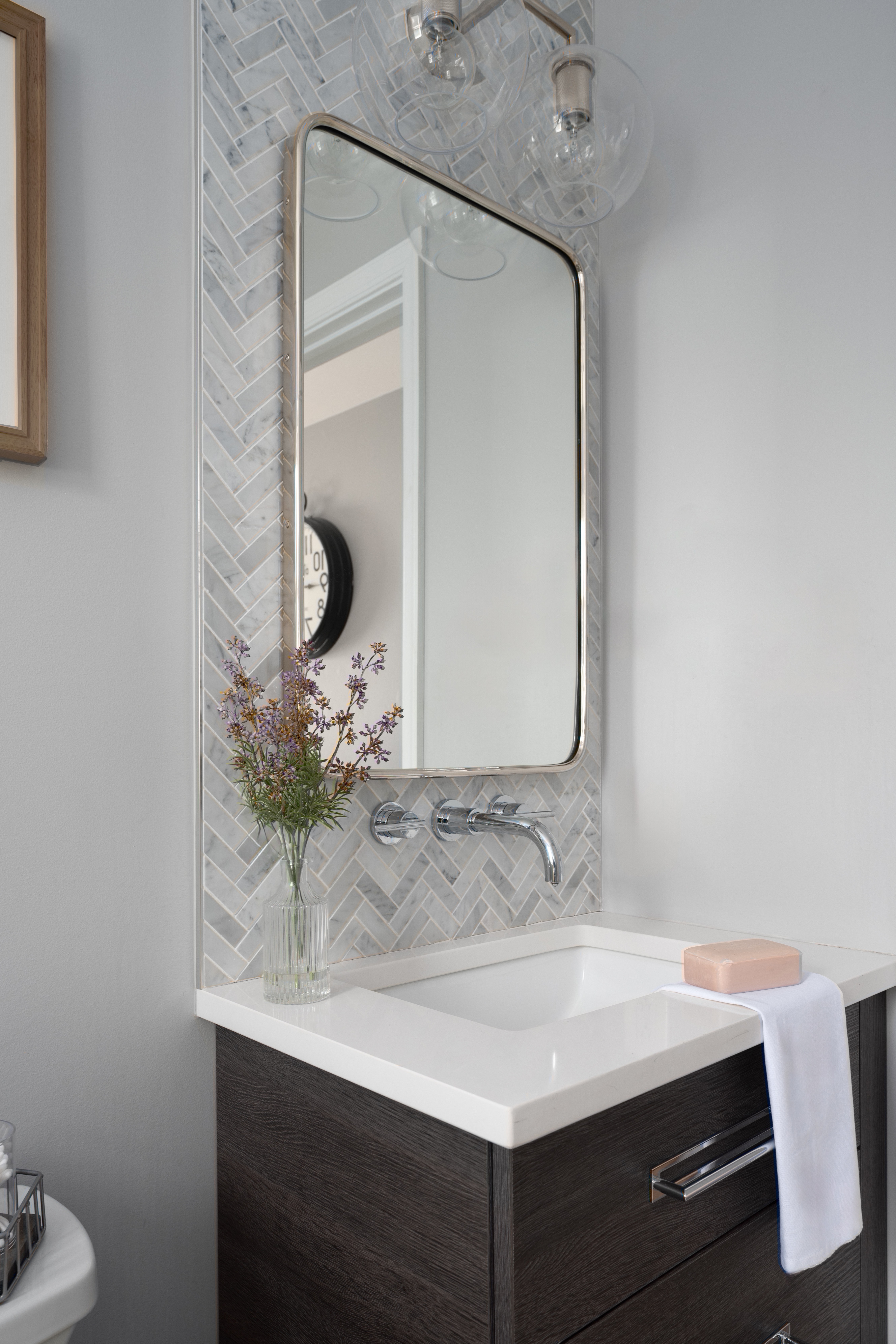 a white and gray themed bathroom with cool gray tiles and a silver-rimmed rectangular mirror above the white sink
