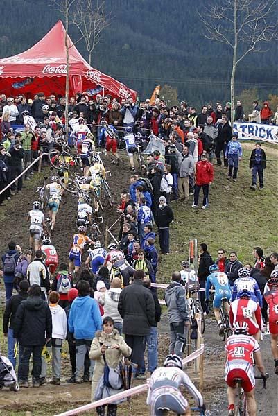 Fans watch the racers scramble up a muddy hill.