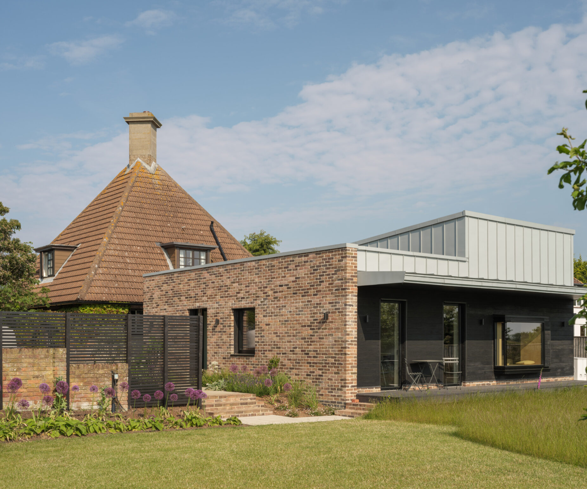 modern flat roof extension to pitched roof house with metal cladding, raised roof section and brick wall