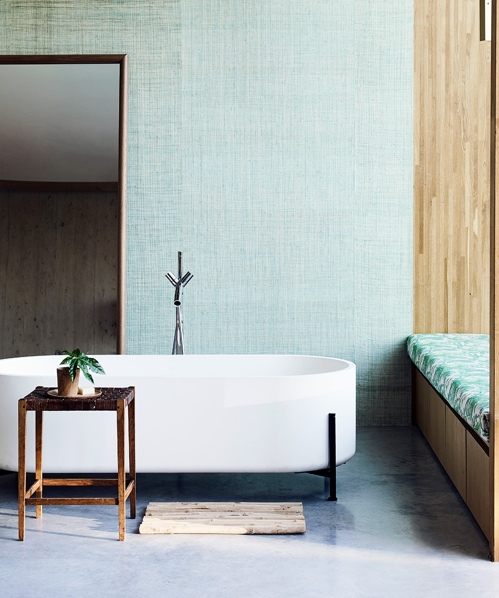 A modern white bath with sleek black legs in front of a green wall