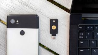 A YubiKey 5C NFC resting on a wooden surface alongside an Android phone and a laptop.