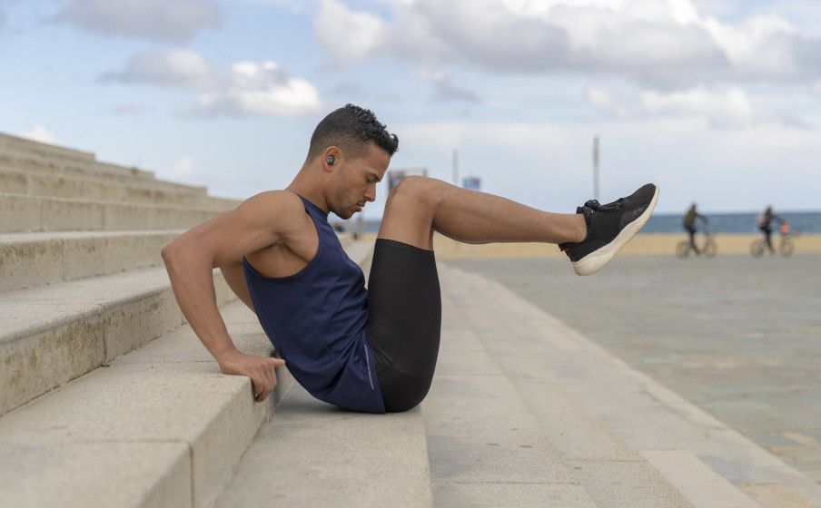 A person doing crunches on large stone steps while wearing the JBL Reflect Flow PRO