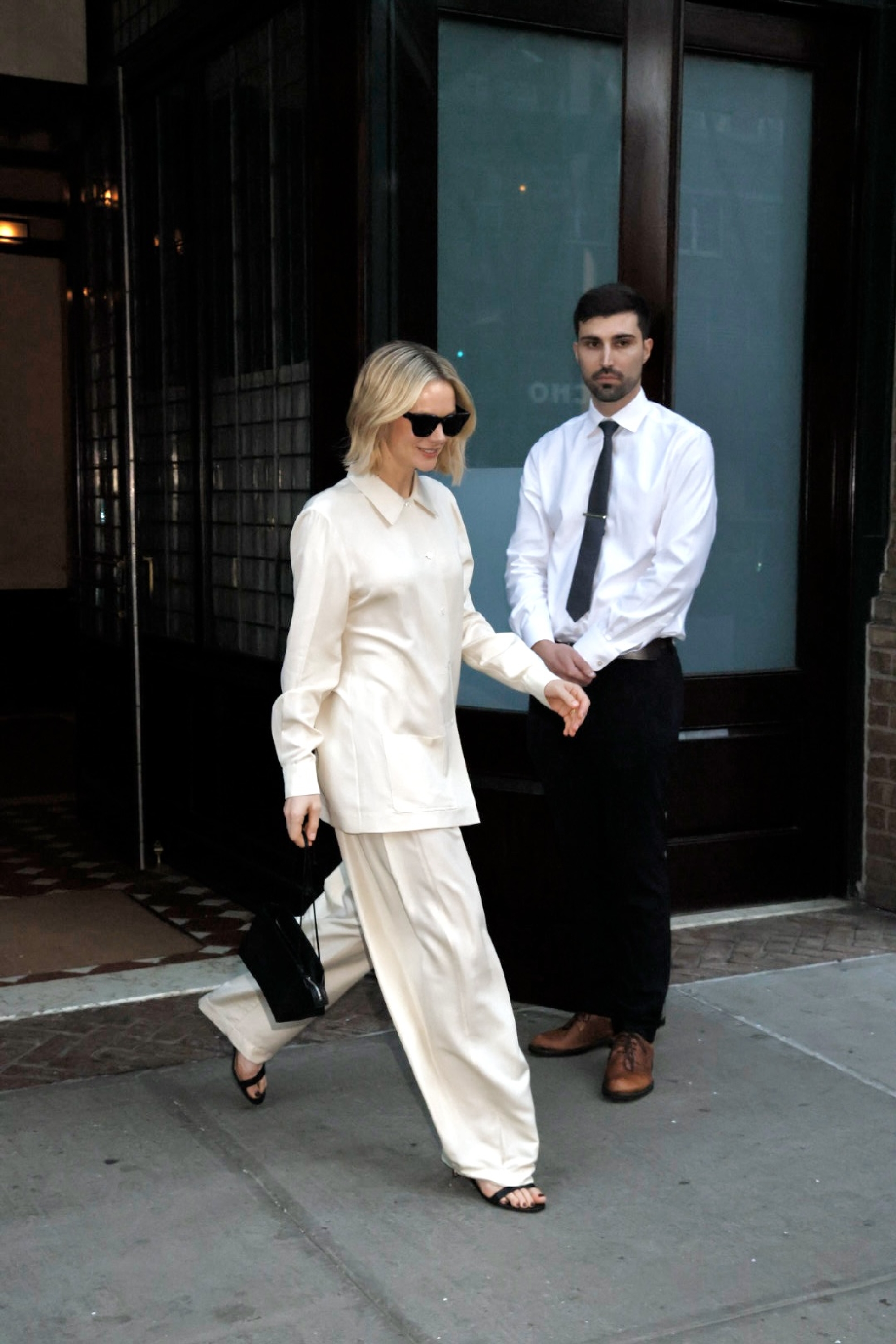 Carey Mulligan steps outside wearing cream trousers with a matching top and black sandals.