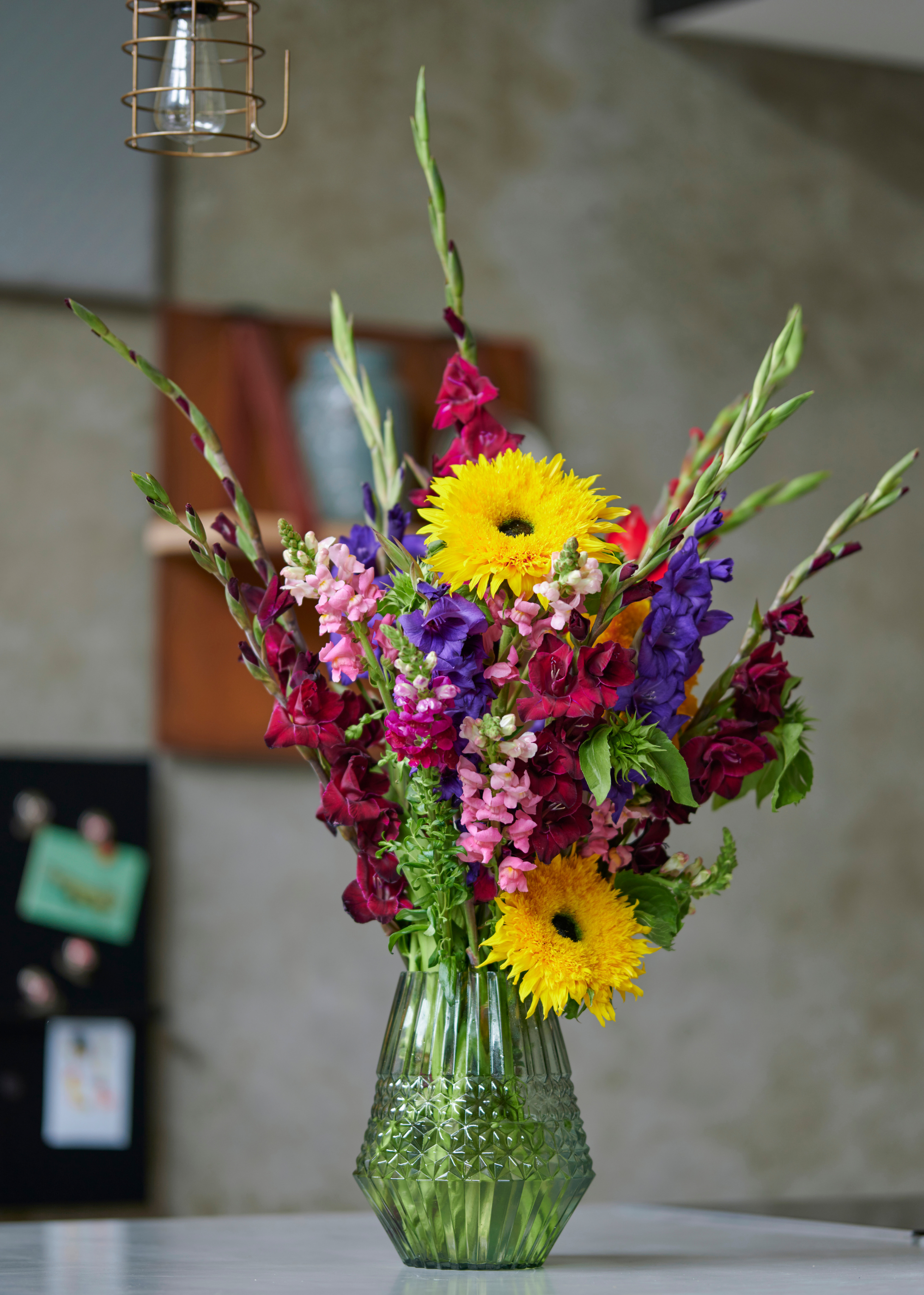 A green vase with gladiolus and other flowers on a kitchen island
