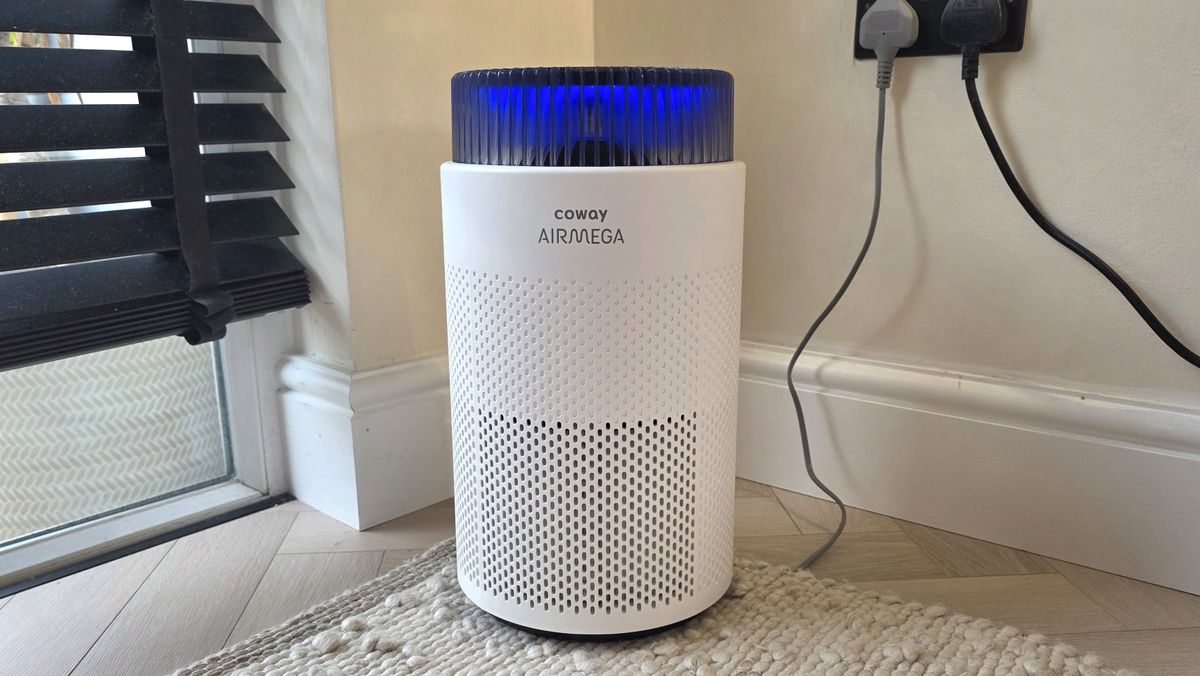 The Coway Airmega 100 standing in the corner of a room near some blinds.