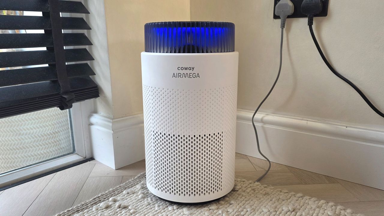 The Coway Airmega 100 standing in the corner of a room near some blinds.