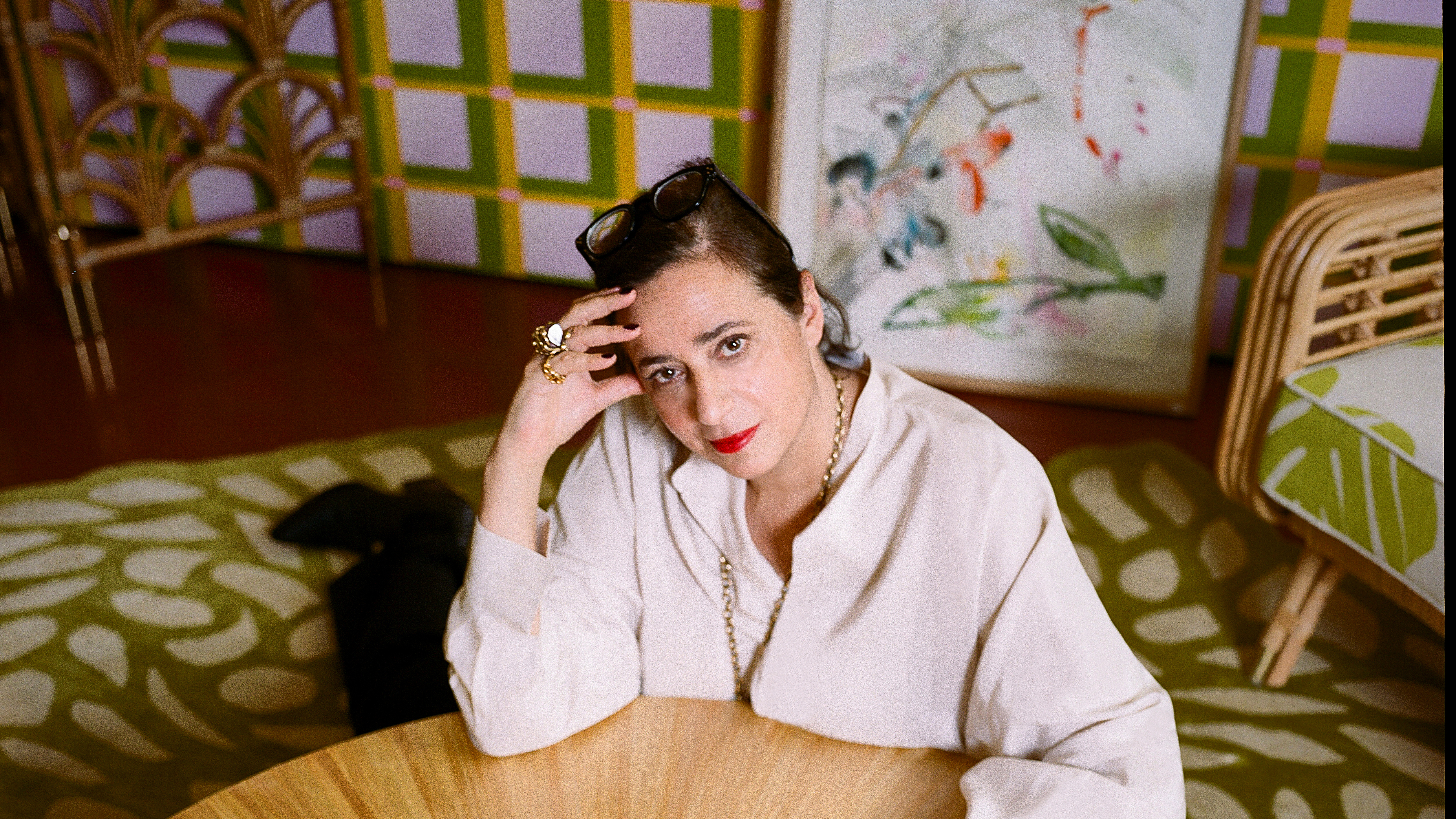 India Mahdavi sat at a table looking to camera with lots of pattern behind her