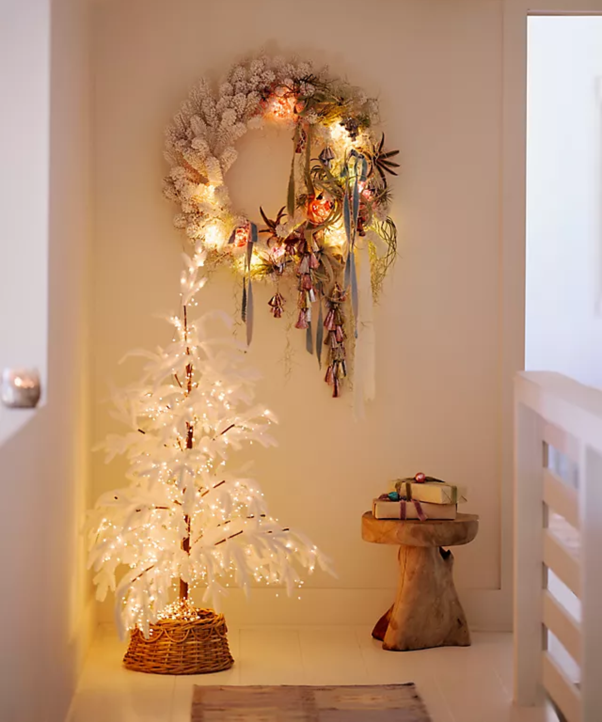 a whimsical, scandi-style Christmas scene with a white tree and a decorative wreath hanging on the wall