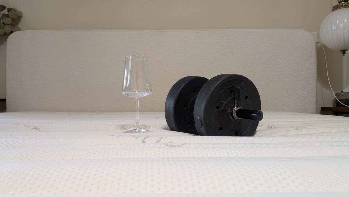 A wine glass and a 15lb weight used for motion isolation tests sit on the surface of the Saatva Zenhaven Latex mattress.