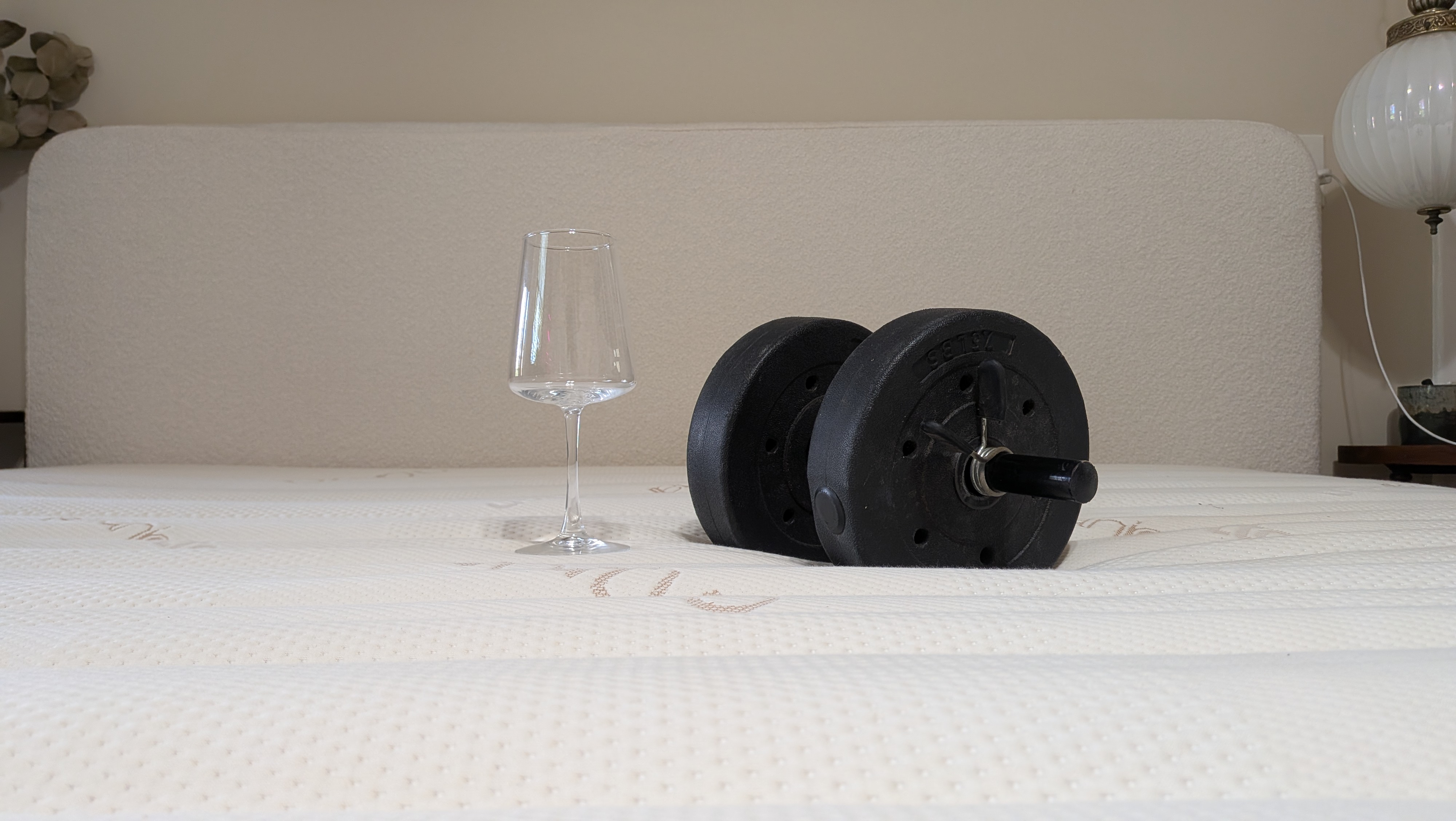 A wine glass and a 15lb weight used for motion isolation tests sit on the surface of the Saatva Zenhaven Latex mattress.