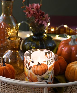 A light brown rattan tray with orange candles, pumpkin candles, and fairy lights on top of it