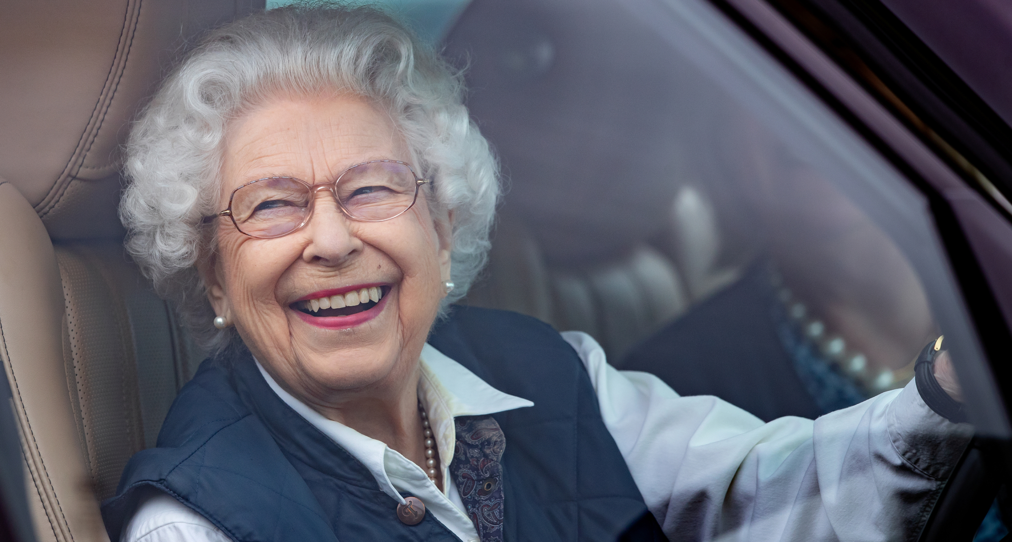 Queen Elizabeth laughing driving a car