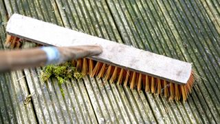 Wooden long handled brush with stiff orange bristles sweeping algae off grooved wooden decking