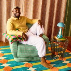 Designer Yinka Ilori sitting on a patterned green swivel chair he's designed for Dunelm surrounded by other pieces from the range