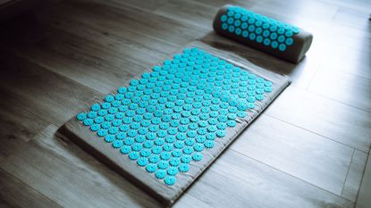 Grey accupressure mat and head rest with blue round pressure points on wooden floor