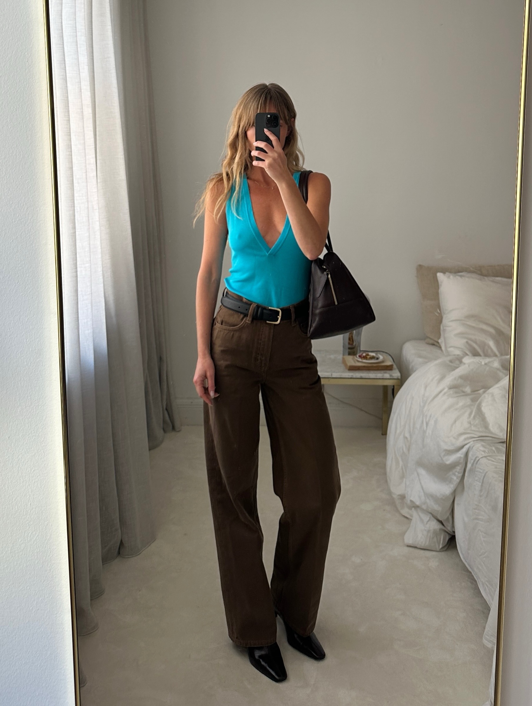Colourful capsule wardrobe autumn 2026: _jeanettemadsen_ wears an aqua top. She styles it with brown trousers, black boots, a black belt and a black bag. This image was taken from Instagram recently.