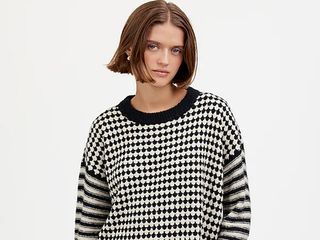 model wears black and white sweater with stripes on sleeves and diamonds on torso and jeans with a studded belt