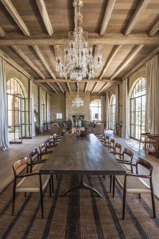 Large dining hall with striped rug and exposed wooden beams, stone fireplace