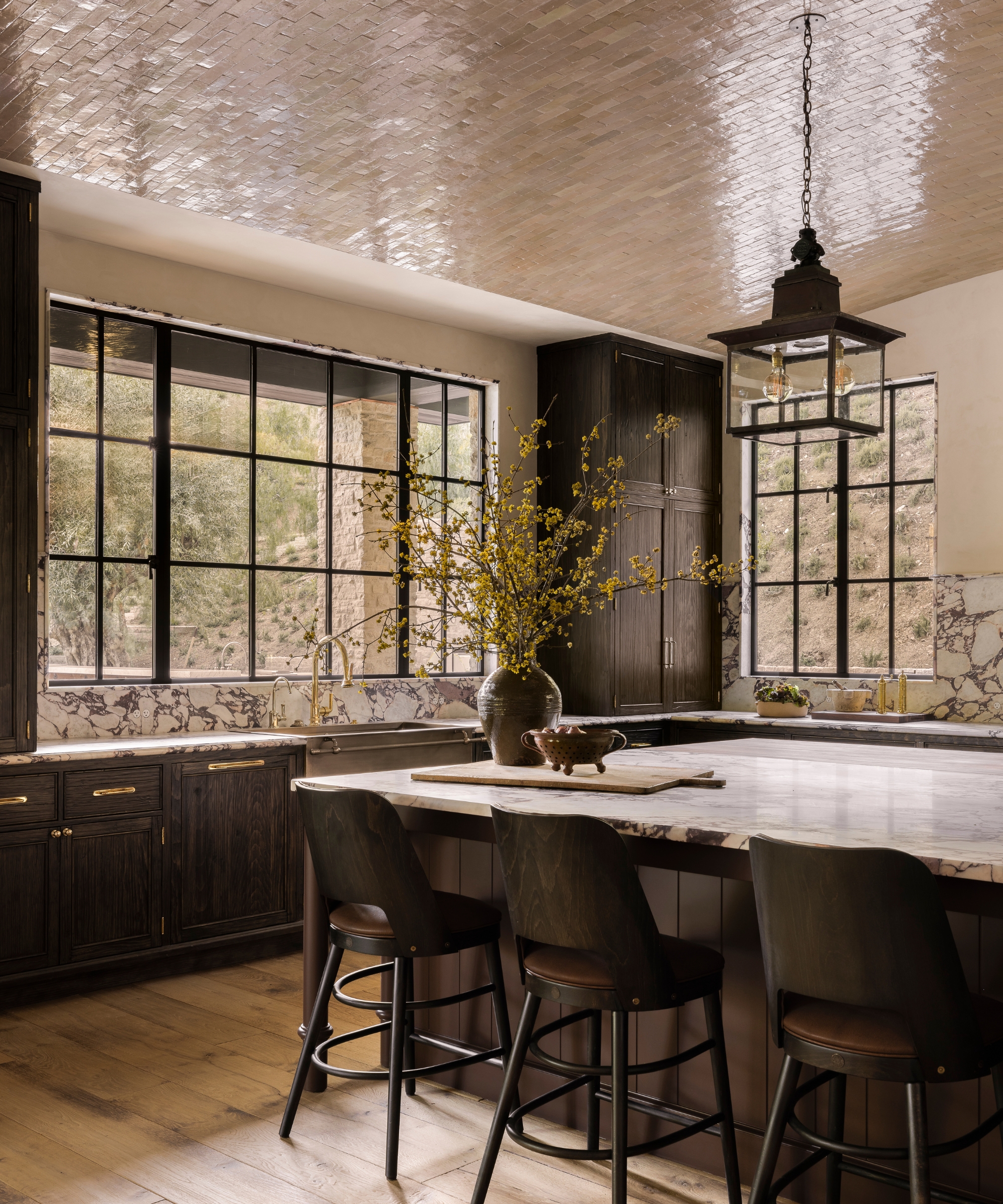 a moody kitchen with dark wood cabinets, marble countertops, a tiled glossy domed ceiling, and brass hardware