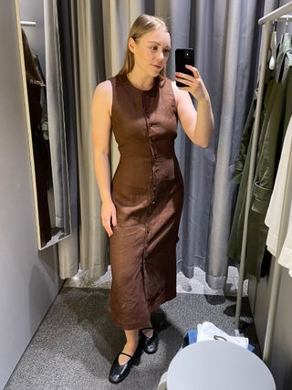 Woman in dressing room wears brown linen dress and black ballet flats