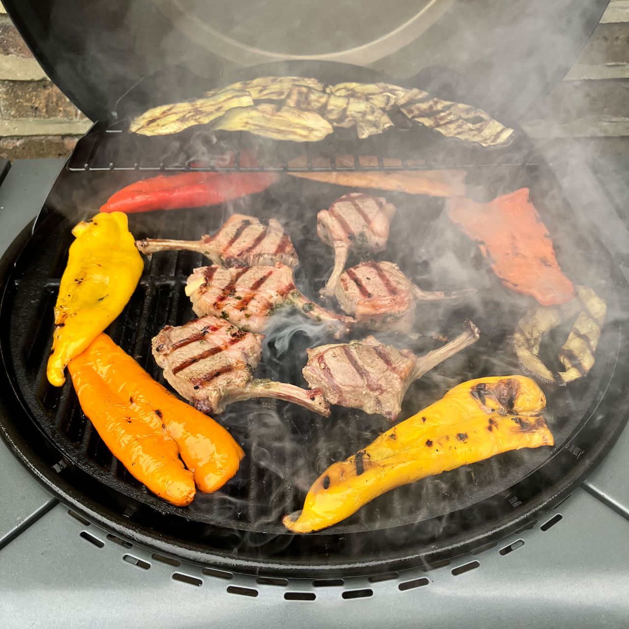a close up of a barbecue grill with lamb chops and grilling vegetables