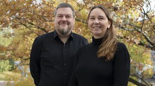 A man and woman smiling in front of an autumn-colored tree about their new positions at Genelec.
