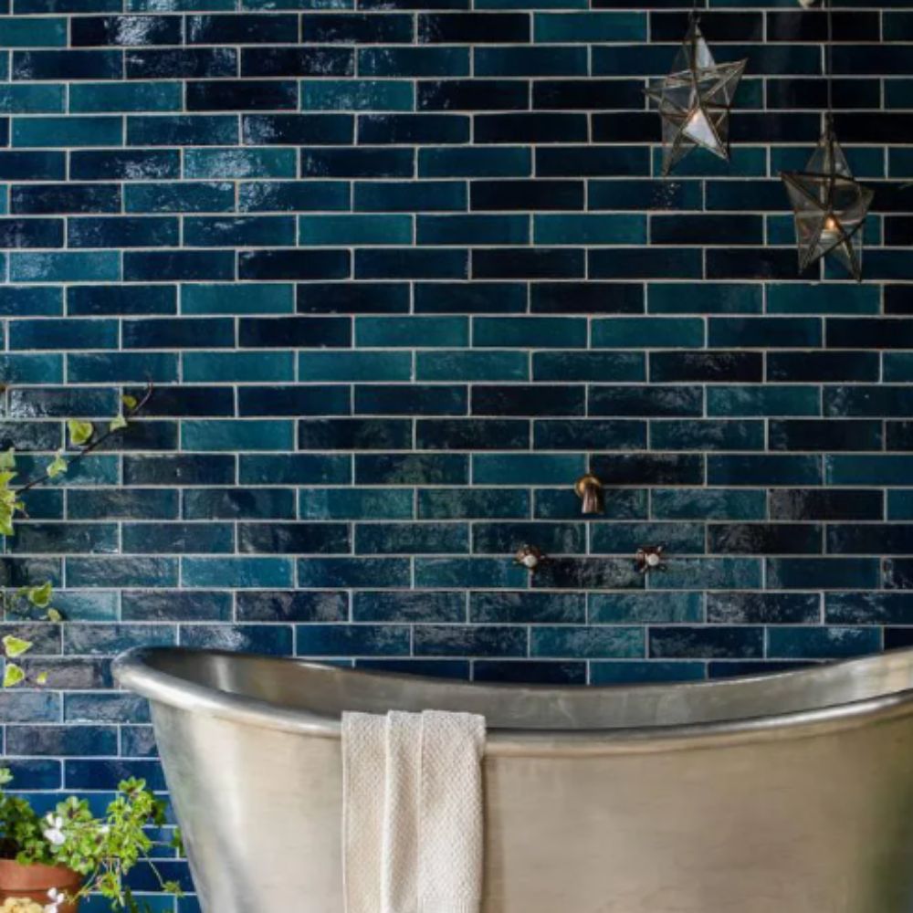 A deep teal metro-tiled bathroom wall with a freestanding silver bath, trailing plants and hanging star lanterns.