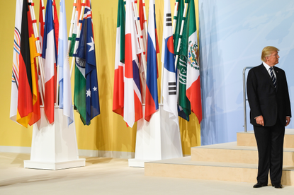 President Trump standing beside international flags. 