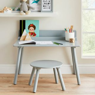 A grey kids desk and matching stool with art supplies on top of the desk