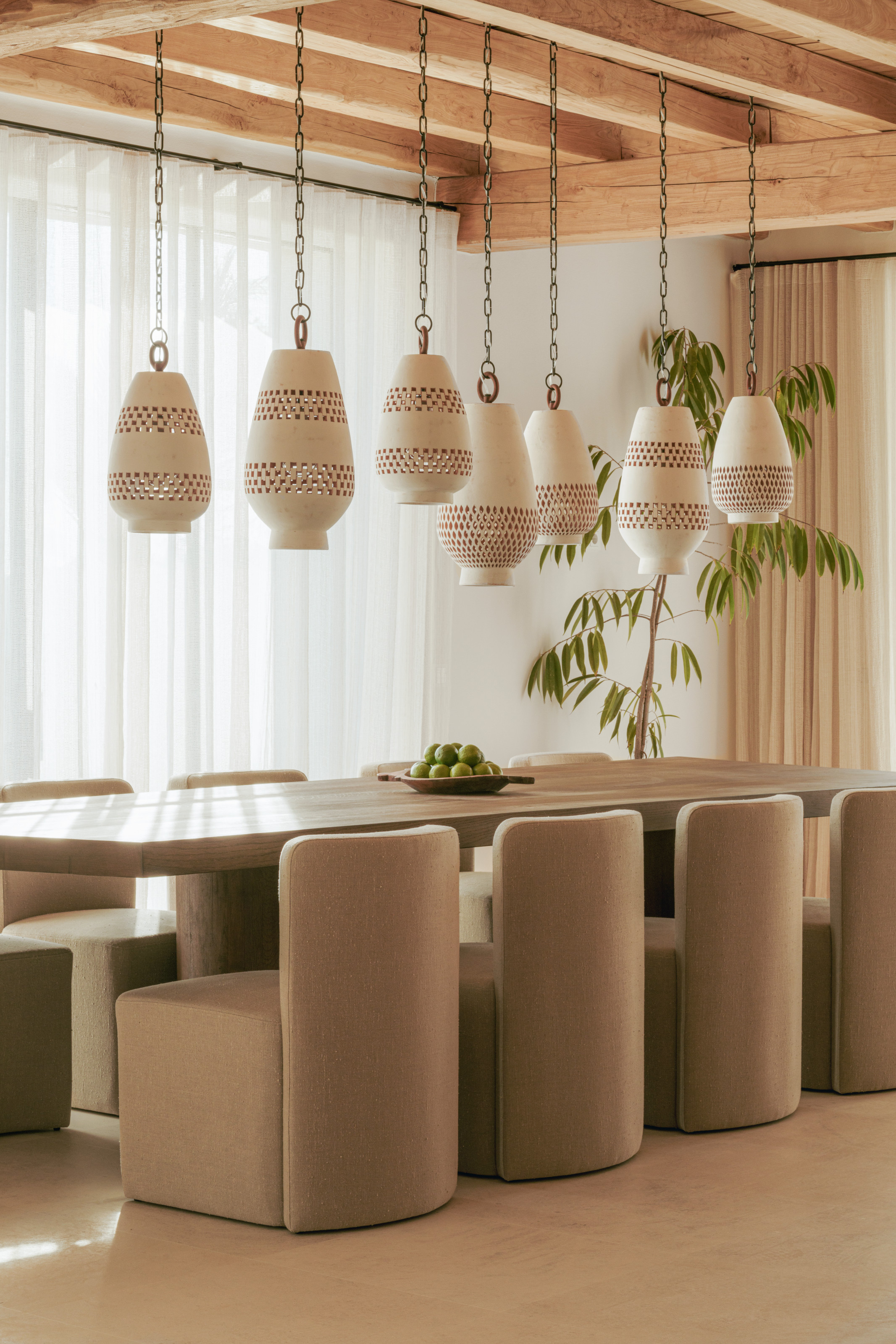 Dining room with custom wooden dining table and upholstered chairs, with seven perforated pendants hanging above