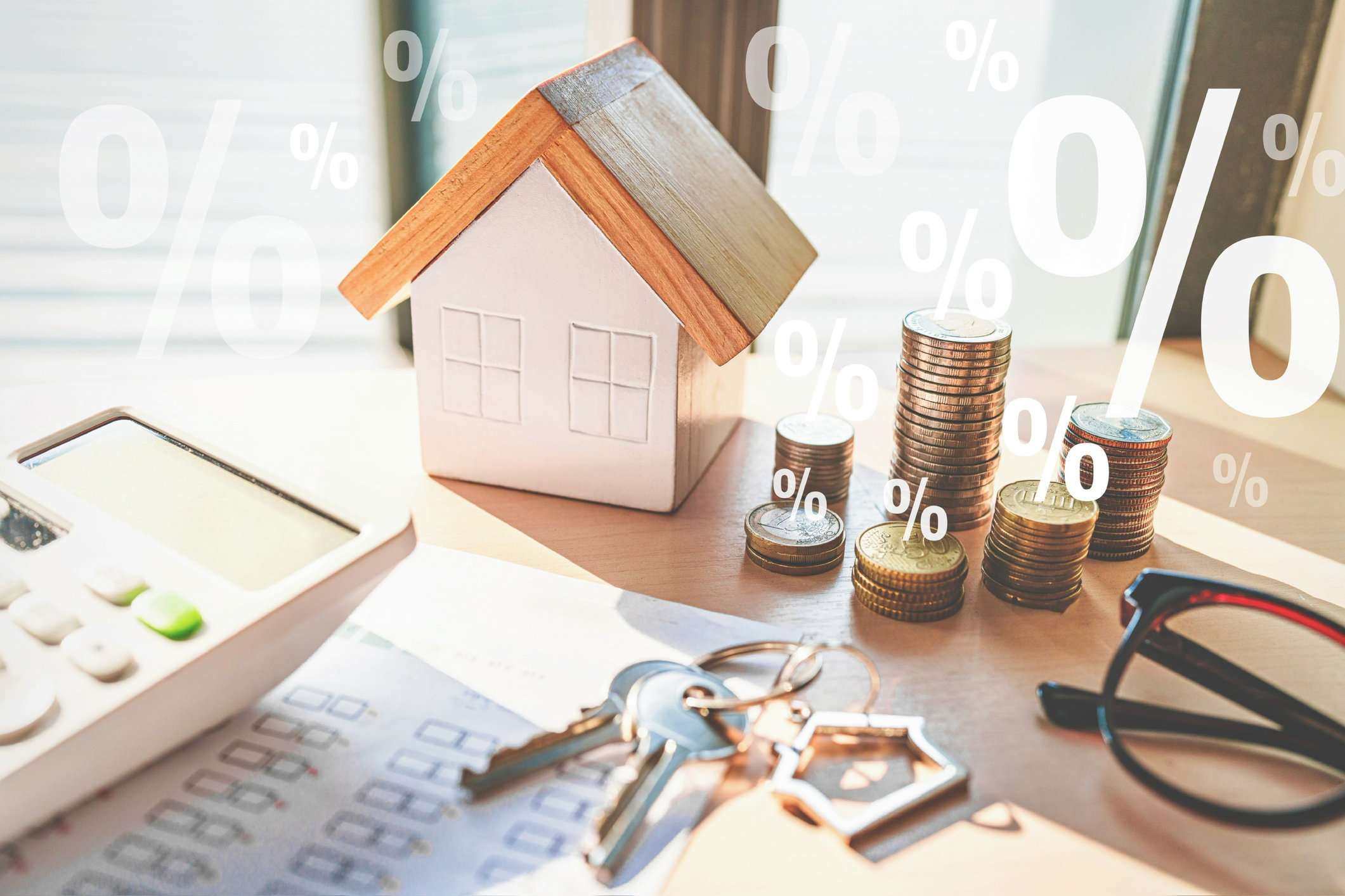 Model house on desk with calculator, house keys, coins and glasses, with percentage symbols superimposed over the photo. Mortgage concept.