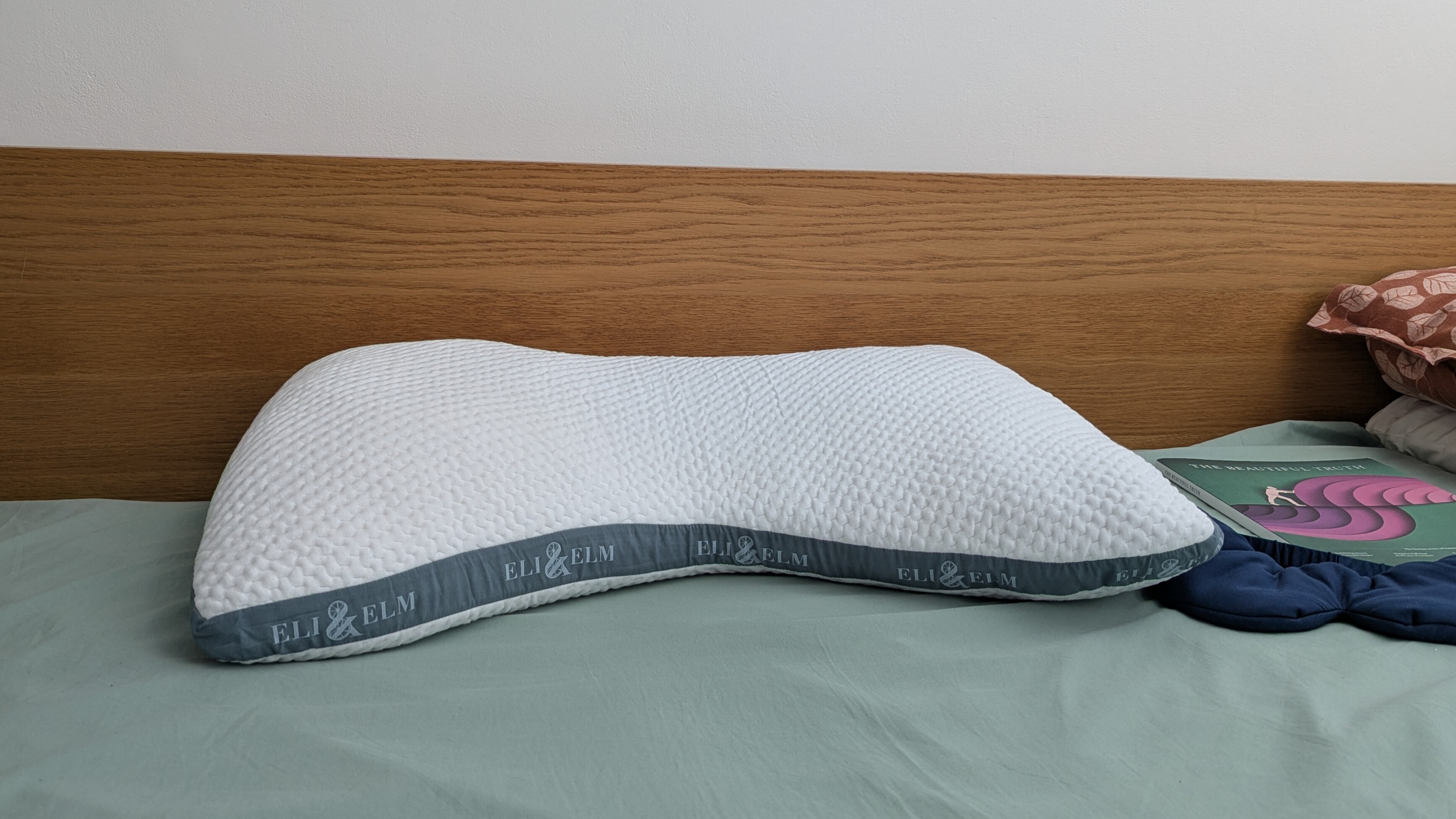 Eli and Elm Side Sleeper Pillow on the bed with a green bedsheet in a brightly lit room 