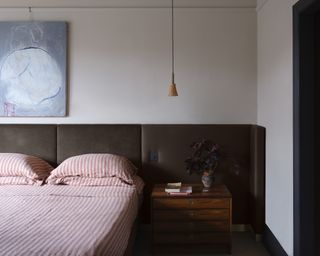 farrow & ball color of the year clay tones in a neutral colored bedroom with a wooden nightstand and red bedding