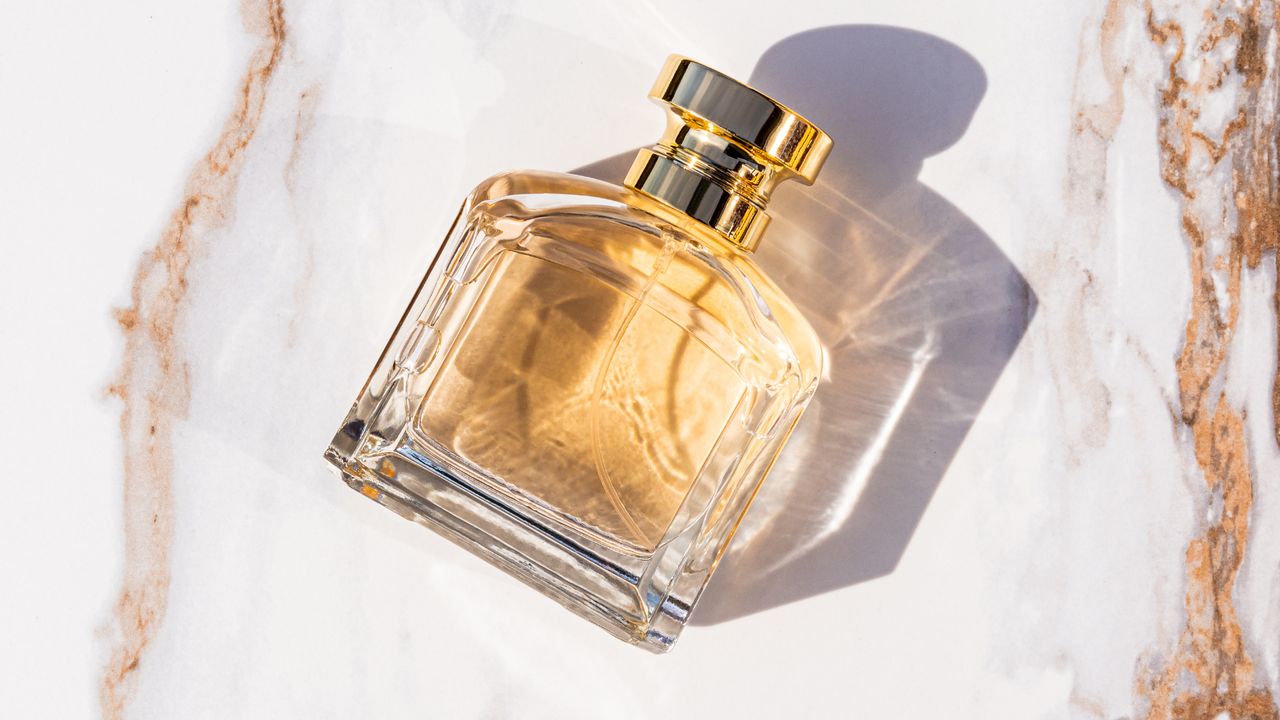 Bird&#039;s eye view of a perfume bottle filled with gold perfume laying on its side against a white and bronze marble counter